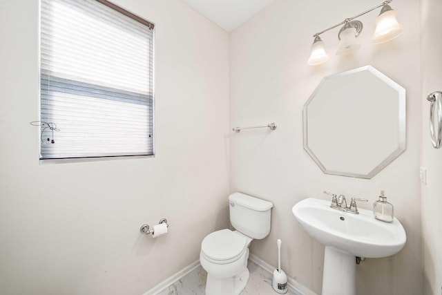 half bathroom with toilet, marble finish floor, and baseboards