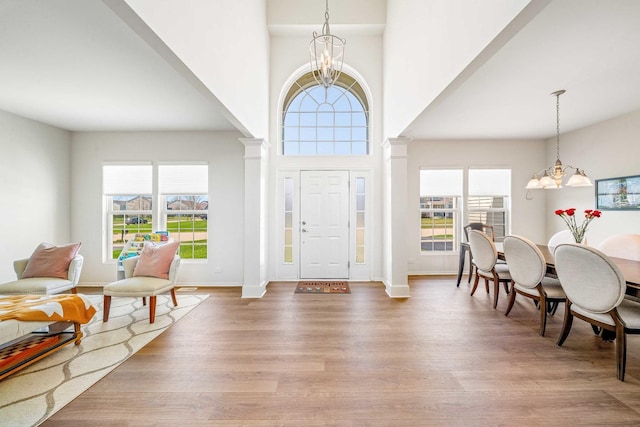 entrance foyer with light wood finished floors, decorative columns, and a notable chandelier