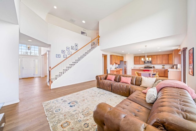 living area with a notable chandelier, recessed lighting, a high ceiling, stairs, and light wood-style floors
