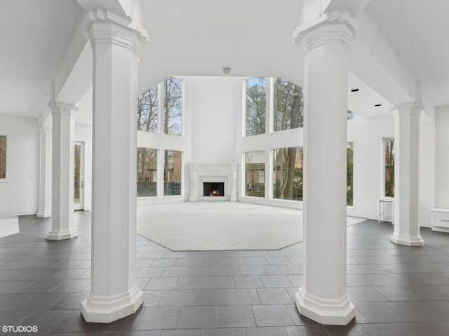 living room featuring decorative columns, a towering ceiling, and a warm lit fireplace