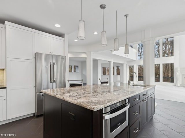kitchen with a sink, open floor plan, appliances with stainless steel finishes, ornate columns, and white cabinetry