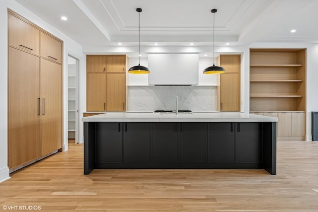 3846 N Bell Ave, Chicago, IL 60618 - kitchen featuring a tray ceiling, light countertops, light wood-style floors, backsplash, and a large island with sink