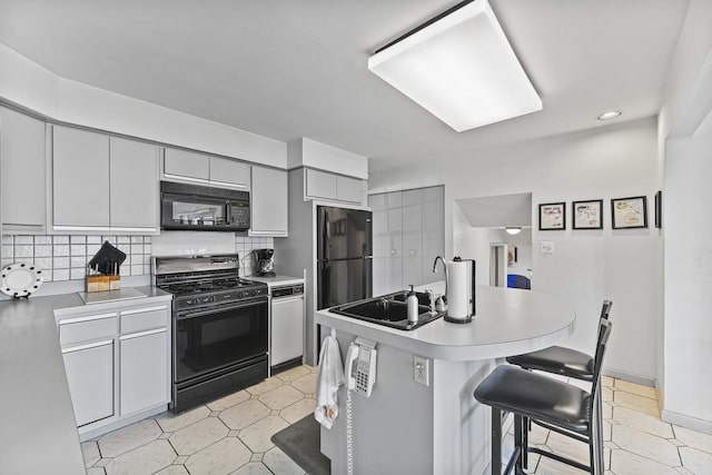 kitchen with a sink, a center island with sink, tasteful backsplash, black appliances, and a breakfast bar area