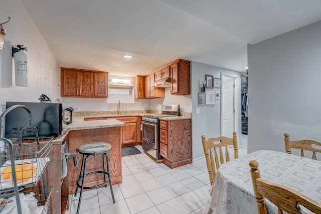 5048 W Wrightwood Ave, Chicago, IL 60639 - kitchen with stainless steel gas range oven, a peninsula, brown cabinets, under cabinet range hood, and light tile patterned flooring