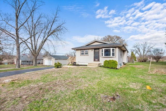 bungalow-style home with an outbuilding, a front yard, a detached garage, and aphalt driveway