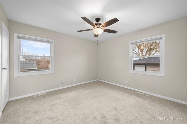 empty room featuring carpet flooring, baseboards, a ceiling fan, and visible vents