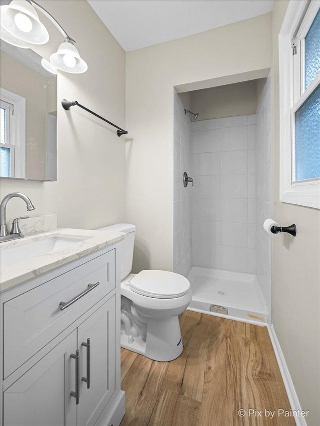 full bath featuring a tile shower, toilet, vanity, and wood finished floors