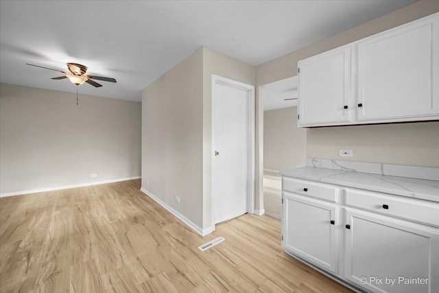 kitchen featuring light wood-style floors, white cabinetry, a ceiling fan, visible vents, and baseboards