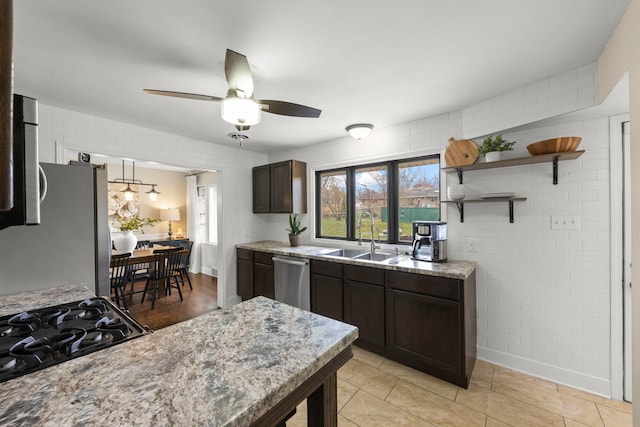 kitchen with a sink, ceiling fan, dark brown cabinetry, stainless steel appliances, and light stone counters