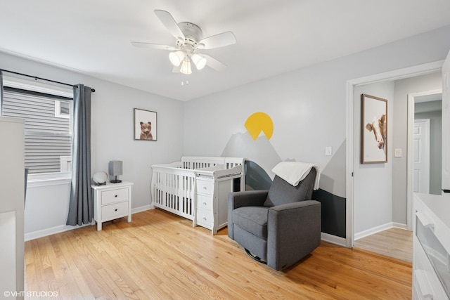 bedroom with a nursery area, baseboards, light wood finished floors, and a ceiling fan