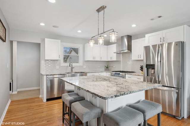 kitchen with stainless steel appliances, visible vents, wall chimney exhaust hood, and a breakfast bar area