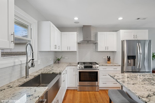 kitchen featuring visible vents, wall chimney exhaust hood, a sink, light wood-type flooring, and stainless steel appliances