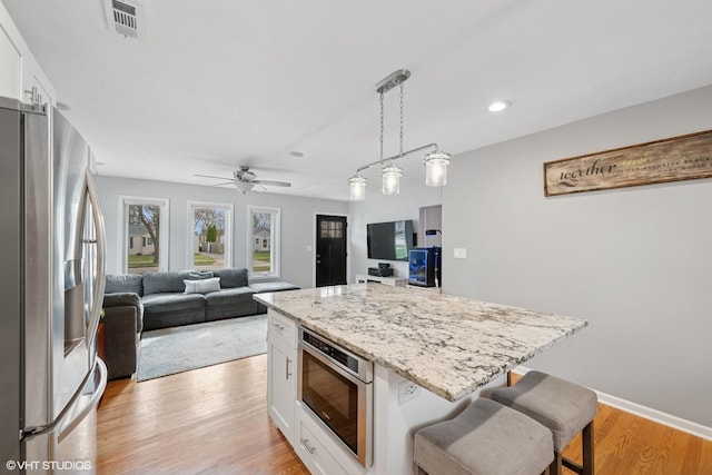 kitchen with stainless steel fridge, light wood-style flooring, white cabinetry, light stone countertops, and visible vents