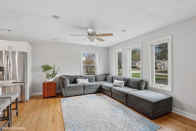 living area with light wood-style floors, visible vents, baseboards, and ceiling fan