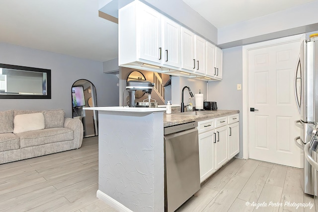 kitchen with white cabinets, a sink, open floor plan, appliances with stainless steel finishes, and light wood-type flooring