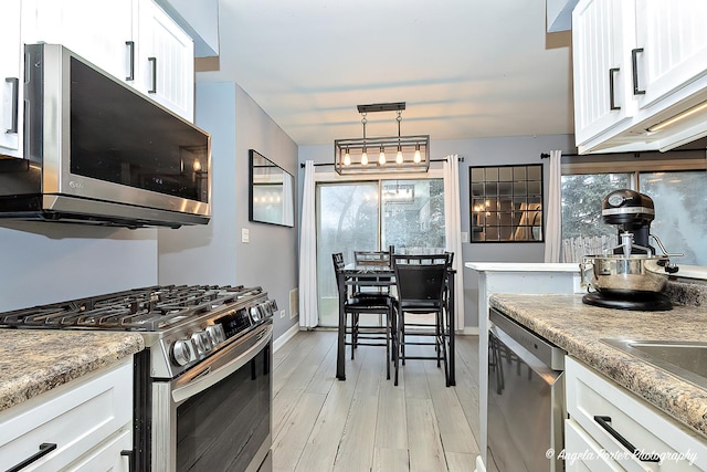 kitchen with stainless steel appliances, white cabinets, light wood-type flooring, and baseboards