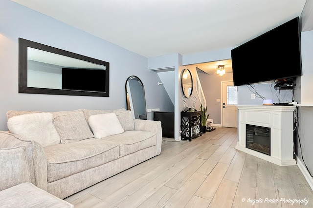 living area featuring light wood-style flooring, baseboards, and a glass covered fireplace