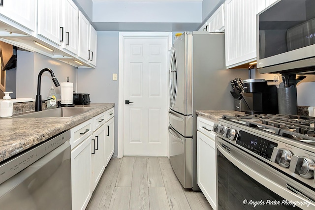 kitchen with white cabinetry, light countertops, a sink, stainless steel appliances, and light wood finished floors