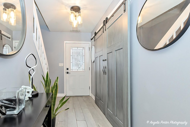 foyer with light wood-type flooring, baseboards, visible vents, and a barn door