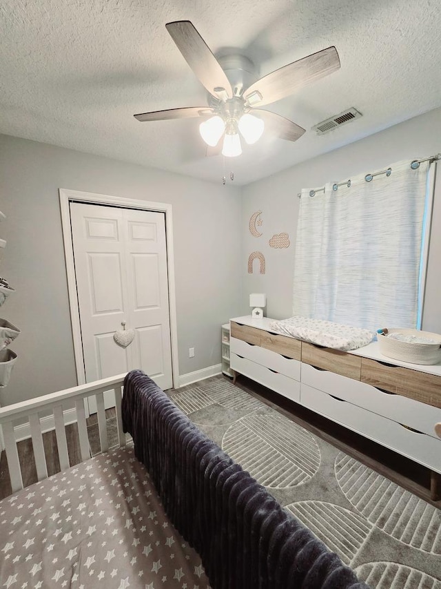 bedroom with baseboards, a closet, a textured ceiling, a ceiling fan, and visible vents