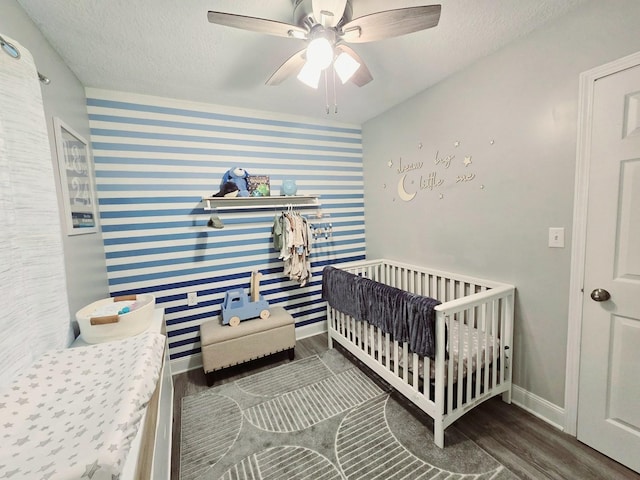 bedroom featuring baseboards, a crib, a textured ceiling, wood finished floors, and wallpapered walls