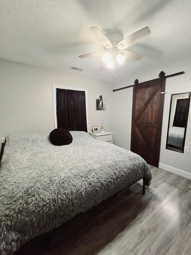 bedroom with a textured ceiling, wood finished floors, visible vents, and a barn door