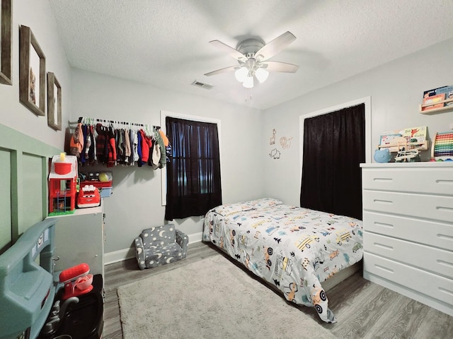 bedroom with visible vents, baseboards, wood finished floors, and a textured ceiling