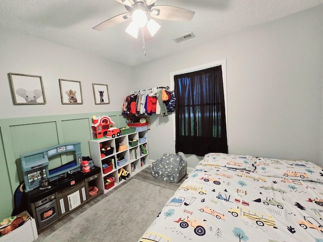 bedroom featuring a decorative wall, visible vents, a textured ceiling, and ceiling fan