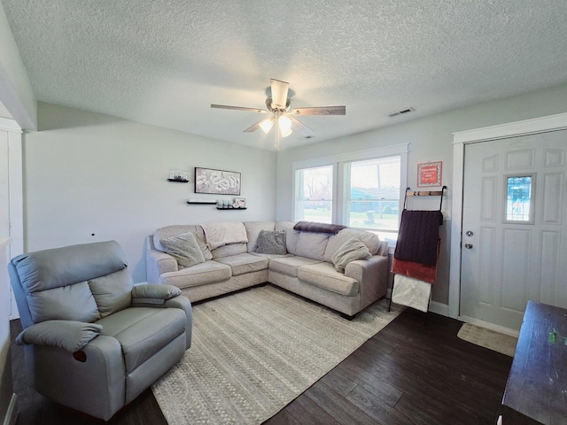 living area featuring dark wood-type flooring, visible vents, a textured ceiling, and ceiling fan