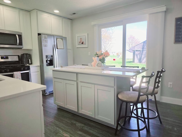 kitchen featuring visible vents, a kitchen island, appliances with stainless steel finishes, light countertops, and dark wood-style floors