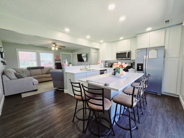 kitchen with a sink, light countertops, appliances with stainless steel finishes, a peninsula, and dark wood-type flooring