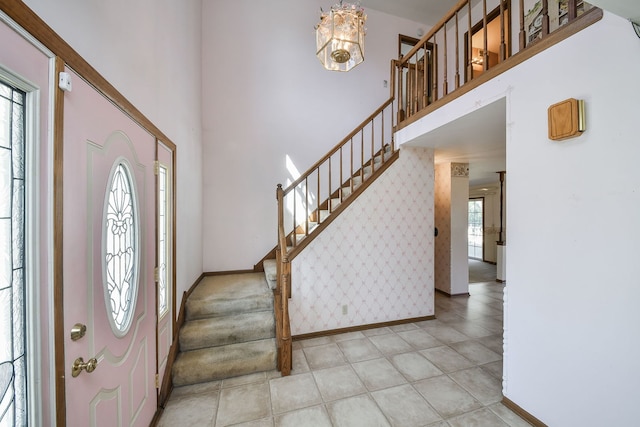 foyer entrance with wallpapered walls, a towering ceiling, baseboards, and stairway