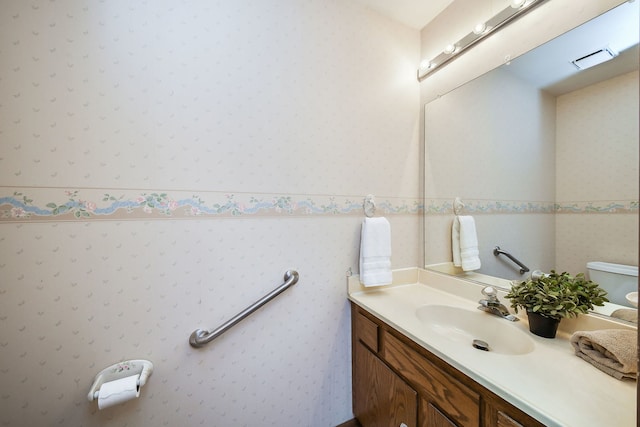 bathroom featuring vanity, wallpapered walls, and toilet