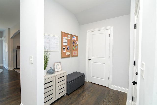 hall with arched walkways, dark wood-type flooring, baseboards, and vaulted ceiling