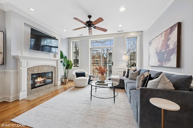 living area with wainscoting, visible vents, crown molding, and wood finished floors