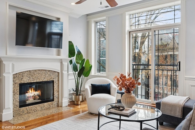 living area featuring ceiling fan, a fireplace, ornamental molding, visible vents, and wood finished floors