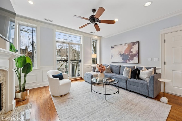living room with a decorative wall, light wood-style flooring, crown molding, and a premium fireplace