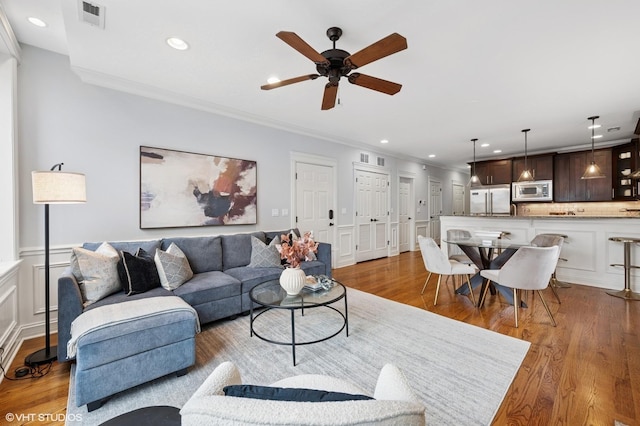 living room with visible vents, a decorative wall, ornamental molding, light wood-type flooring, and a ceiling fan