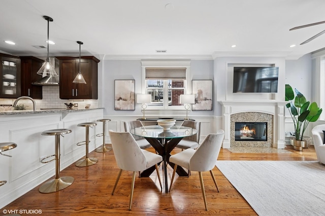 dining space with wood finished floors, ornamental molding, a fireplace, and wainscoting