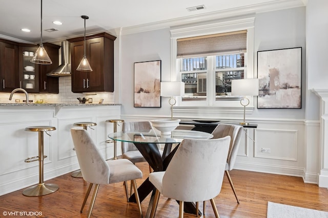 dining space featuring light wood-style floors, a decorative wall, visible vents, and crown molding