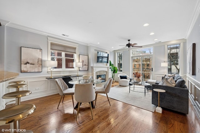 dining area featuring a glass covered fireplace, crown molding, a ceiling fan, and wood finished floors