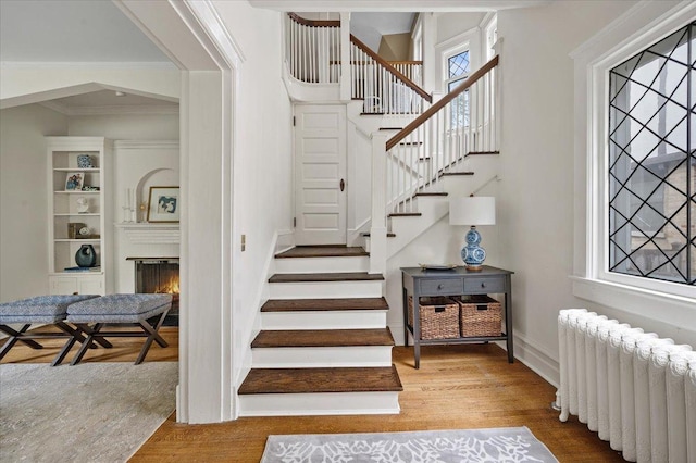 820 Lake Ave, Wilmette, IL 60091 - stairs featuring radiator heating unit, wood finished floors, a warm lit fireplace, baseboards, and crown molding