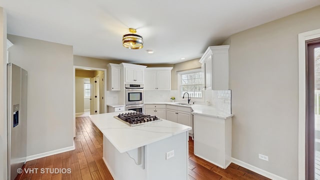kitchen featuring baseboards, appliances with stainless steel finishes, hardwood / wood-style flooring, backsplash, and a kitchen island