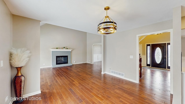 unfurnished living room featuring a glass covered fireplace, baseboards, an inviting chandelier, visible vents, and wood finished floors