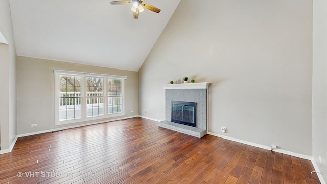 unfurnished living room with high vaulted ceiling, ceiling fan, wood-type flooring, a brick fireplace, and baseboards