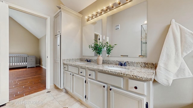 full bath with visible vents, double vanity, a sink, and vaulted ceiling