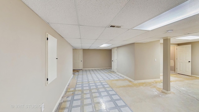 finished basement featuring visible vents, baseboards, a drop ceiling, and light floors