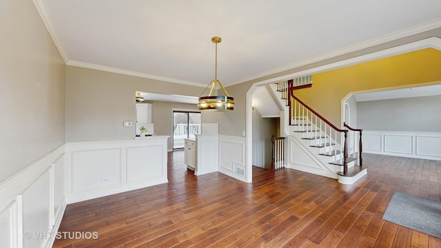 unfurnished dining area with a decorative wall, crown molding, wainscoting, wood finished floors, and stairs