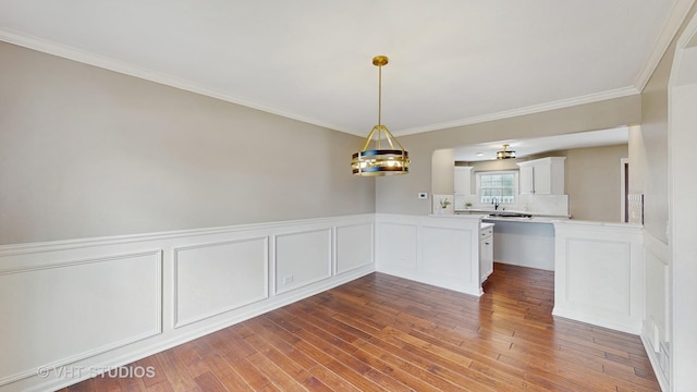 interior space featuring hanging light fixtures, white cabinets, ornamental molding, light countertops, and wood finished floors