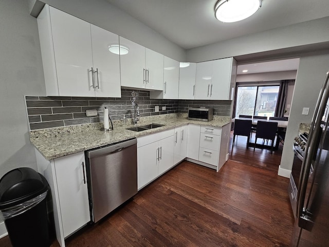 kitchen featuring dark wood finished floors, light stone countertops, appliances with stainless steel finishes, a sink, and backsplash